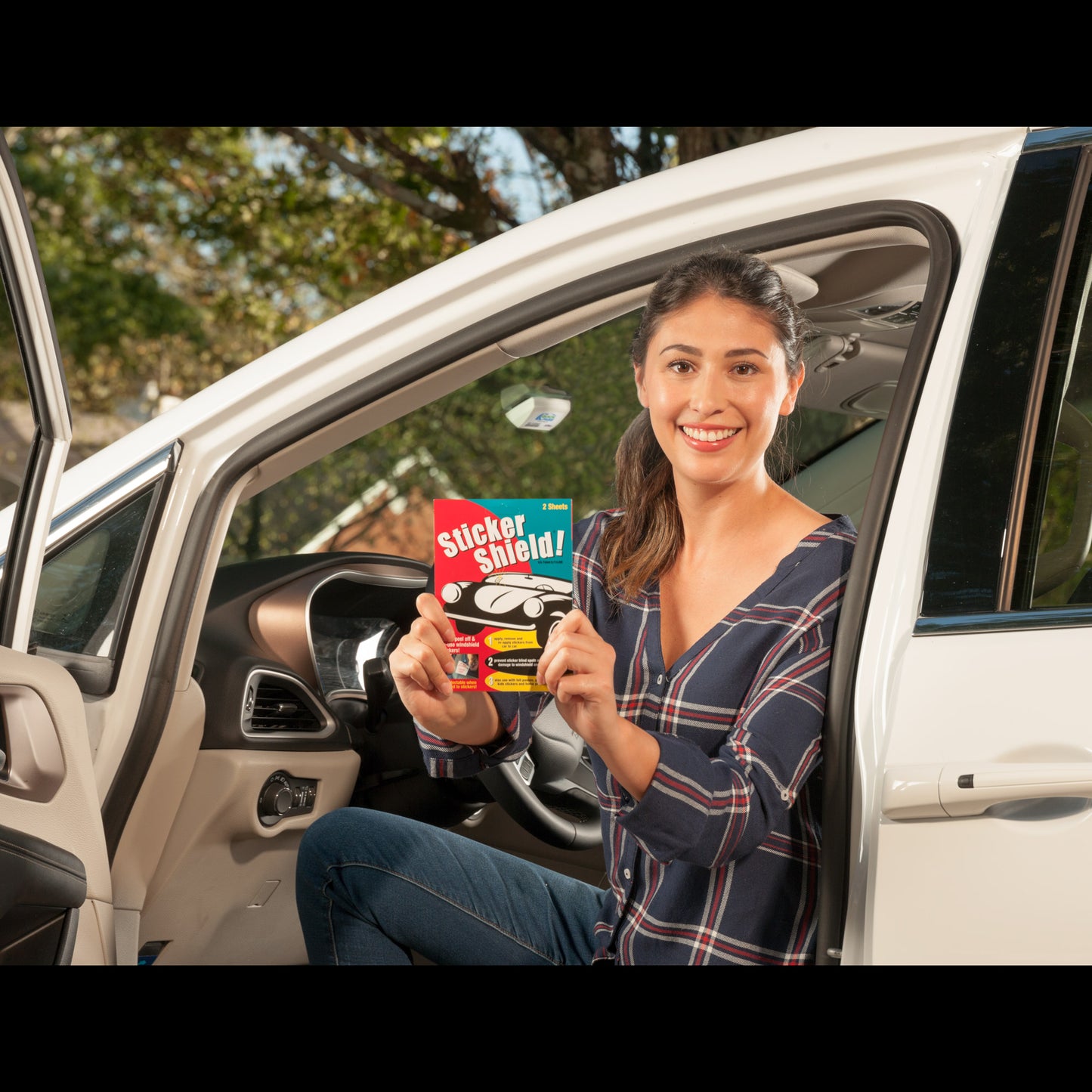 A satisfied customer shows off a pack of sticker shield with her newly placed toll transponder on windshield behind her.