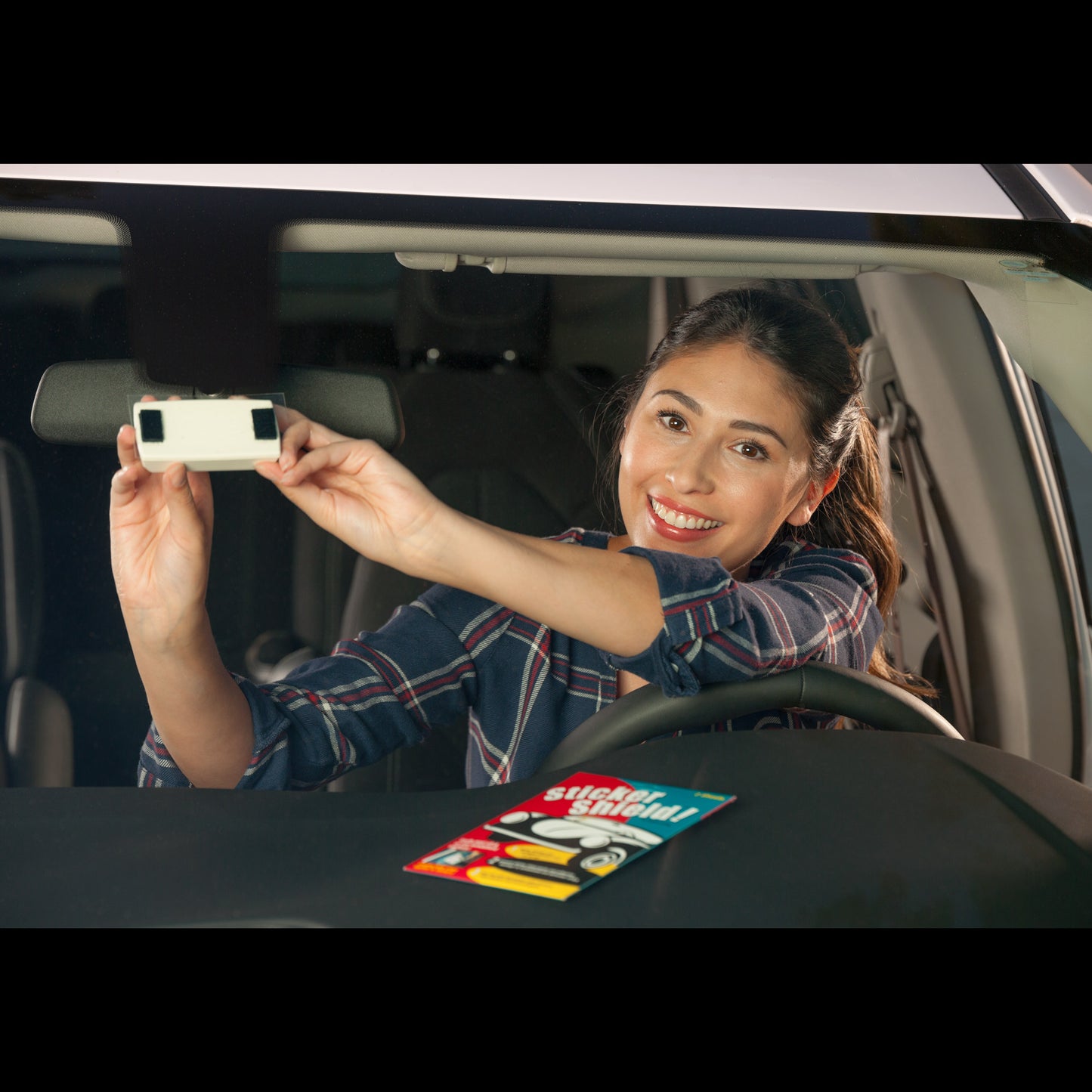 A woman sticks a toll transponder to her windshield using sticker shield.