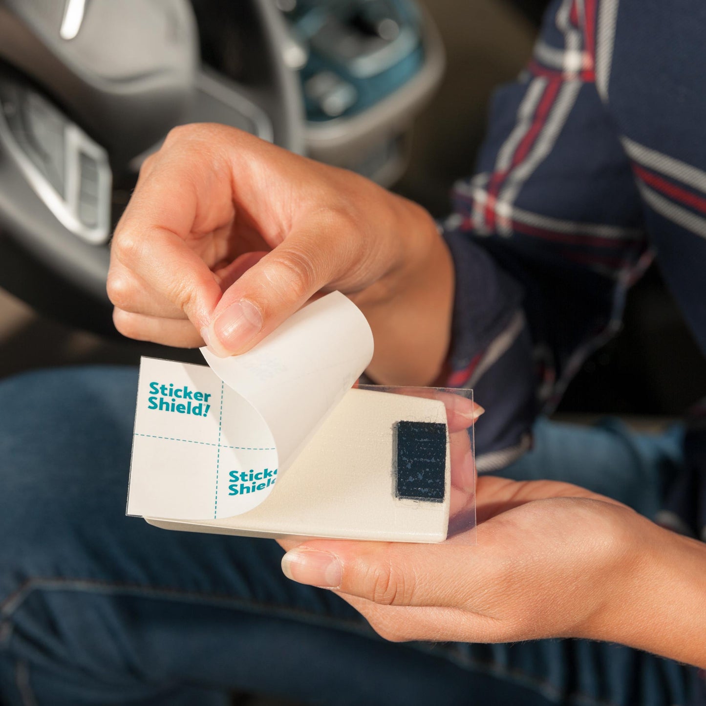 A person peels back the protective liner revealing the adhesive side of sticker shield before applying the toll transponder to the windshield.